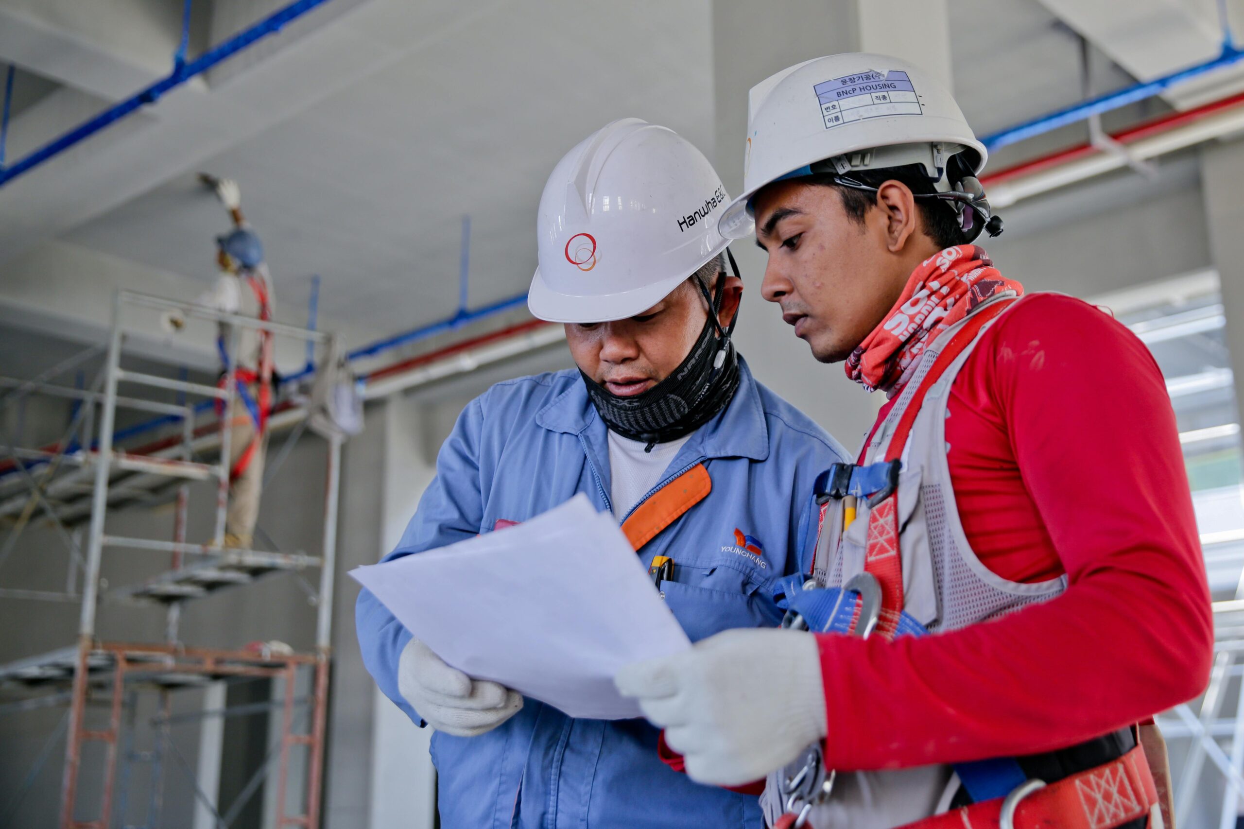 Services Two engineers in safety helmets reviewing construction plans at a worksite.