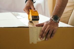 pexels photo 4247758 4247758 Side view of concentrated crop ethnic male sticking cardboard box with tape during preparing for moving in house at daytime